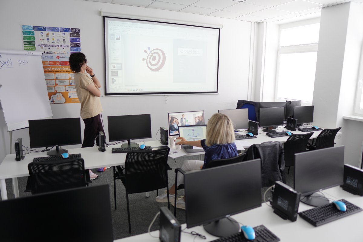 Priebeh kurzu Platená reklama Facebook a Instagram - učebňa s projektorom zobrazujúcim target ikonu, počítače a infografiky o marketingu